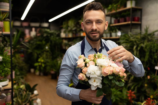 een man in een schort met een boeket bloemen voor een tuinwinkel. - Foto, afbeelding