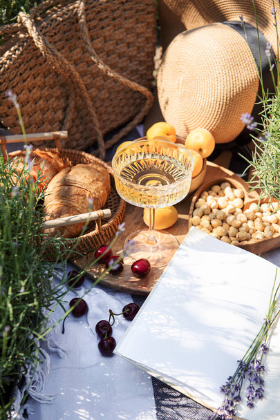Summer picnic on a lavender field with champagne glasses, croissants, apricots and cherry berries - Фото, изображение