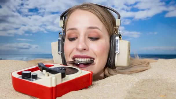 Egy csinos nő a fejéig eltemetve a tengerparton, aki bakelitet próbál tenni egy lemezjátszóra a szájával. - Felvétel, videó