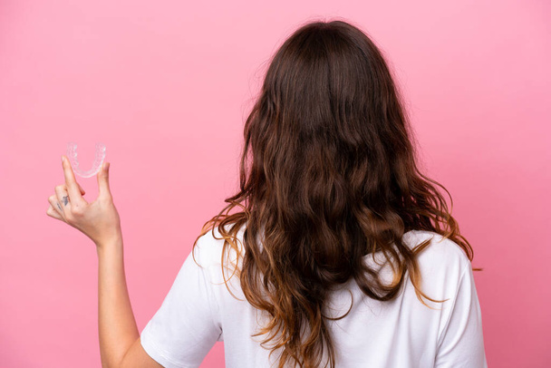 Молода біла жінка тримає невидимі брекети ізольовані на рожевому тлі в положенні спини
 - Фото, зображення