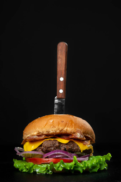 Burger served with knife on black copy space background - Фото, изображение