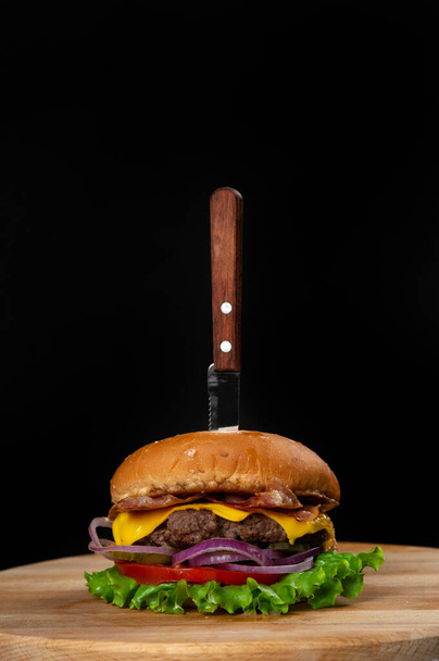 Burger served with knife on black copy space background - Fotó, kép