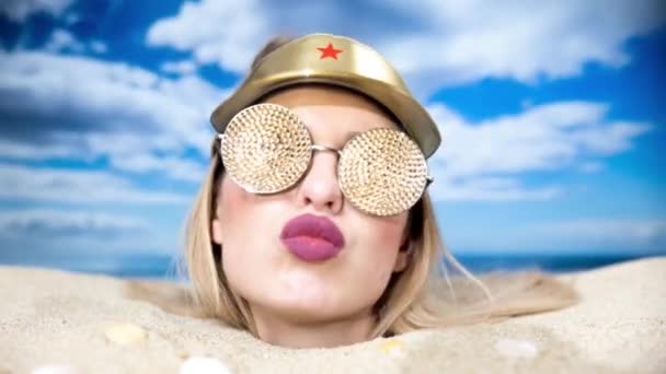 Una mujer bonita enterrada hasta la cabeza en una playa con parasol y gafas de sol brillantes - Imágenes, Vídeo