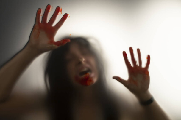 Horror ghost woman with blooded hands behind the matte glass. Halloween festival concept. - Φωτογραφία, εικόνα
