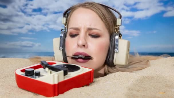 Egy csinos nő a fejéig eltemetve a tengerparton, aki bakelitet próbál tenni egy lemezjátszóra a szájával. - Felvétel, videó