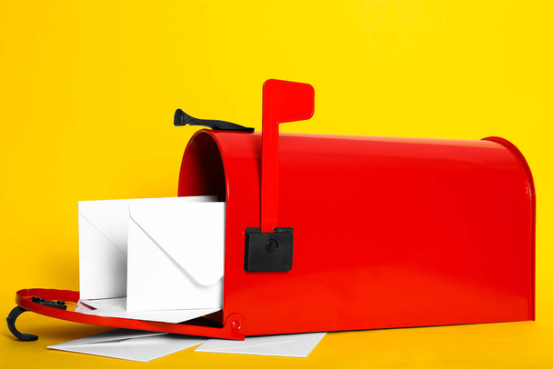 Open red letter box with envelopes on yellow background, closeup - 写真・画像
