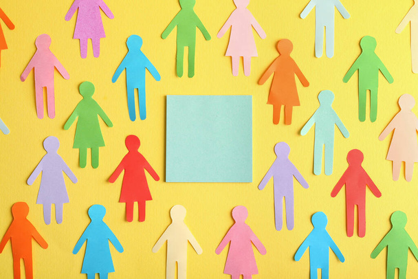 Many different paper human figures around blank card on yellow background, flat lay with space for text. Diversity and inclusion concept - Foto, afbeelding
