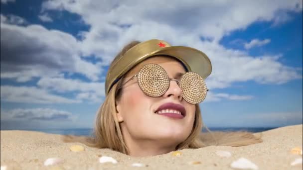 Uma mulher bonita enterrada até a cabeça em uma praia com visor de sol e óculos de sol cintilantes - Filmagem, Vídeo