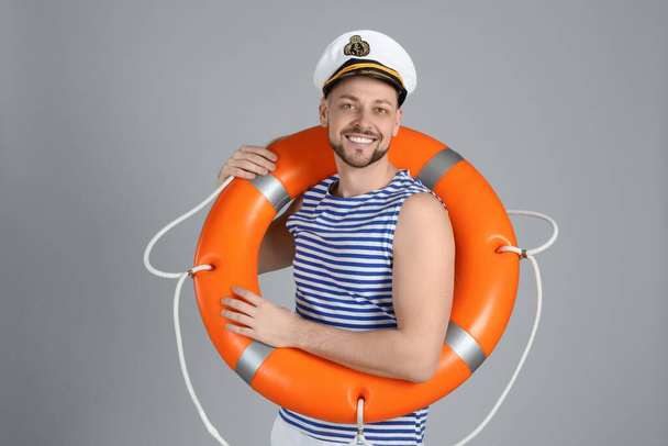 Happy sailor with orange ring buoy on grey background - Foto, Imagem