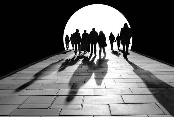 silhuetas de multidão de pessoas caminhando em direção à luz, lançando longas sombras no chão - Foto, Imagem