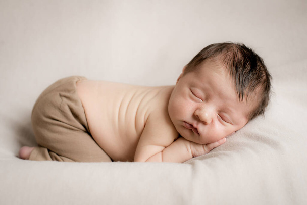 A cute little baby in cute pants sleeps on a beige textile bedspread. Health and motherhood - Foto, Imagem