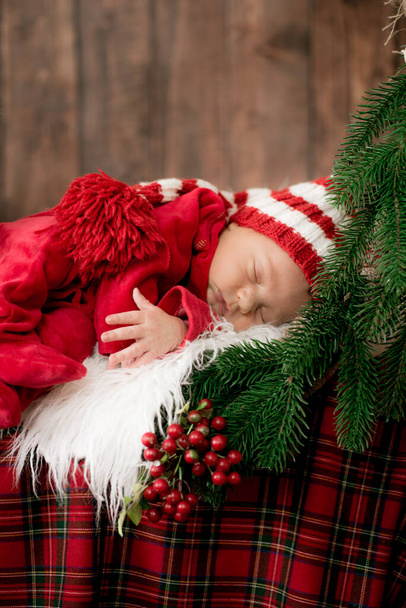 A cute little baby in a red suit and a cap is sleeping in a Christmas decoration. Christmas mood. Happy childhood. - Fotografie, Obrázek
