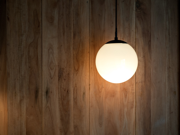 Lâmpada pendurada redonda, forma de lua cheia com a lâmpada no interior brilhando no fundo da parede de madeira na sala escura com espaço de cópia. - Foto, Imagem