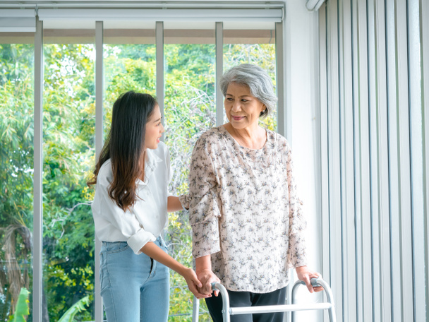 Pflegerin, lächelnde junge Asiatinnen, Tochter oder Enkelin, die älteren Frauen, Müttern oder Großeltern helfen, versuchen mit Rollator zu Hause auf grünem Naturhintergrund zu gehen, Altenpflege. - Foto, Bild