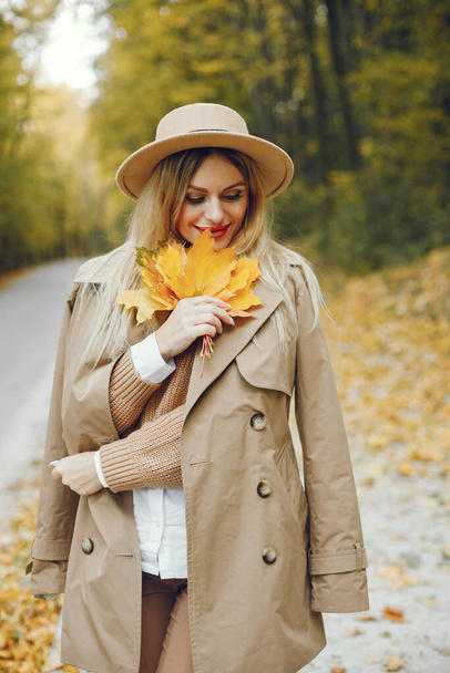 Woman posing for a photo in the autumn park. Caucasian girl has red lips. Woman wearing beige coat and a hat. - Foto, imagen