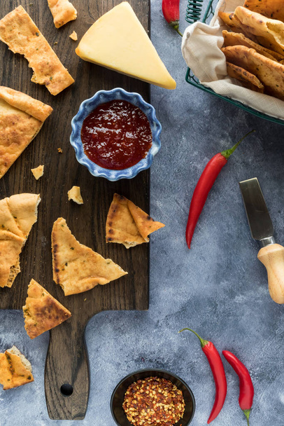 Top down view of a board topped with a bowl of hot pepper jelly and seasoned cracker bread.  - Zdjęcie, obraz