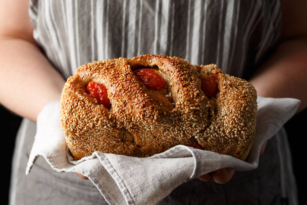 Pan casero fresco con semillas de sésamo y tomates secados al sol en manos de panaderos. - Foto, Imagen