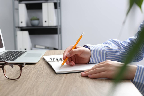 Woman writing in notebook at wooden table in office, closeup - Foto, imagen