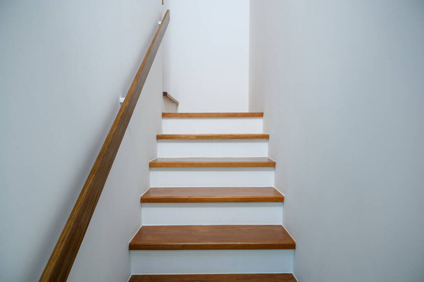 σκάλα ξύλινη με ξύλινες χειρολαβές σε λευκό τοίχο στο σύγχρονο σπίτι. Σχεδιαστική έννοια εσωτερικής δομής. Άδειο μονοπάτι κλιμακοστασίου  - Φωτογραφία, εικόνα