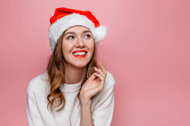 Nahaufnahme Porträt einer jungen glücklich lächelnden Frau mit Weihnachtsmütze isoliert auf rosa Hintergrund im Studio - Foto, Bild