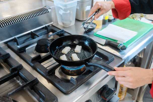 Une femme chef poêle morceaux de saindoux dans la cuisine du restaurant - Photo, image