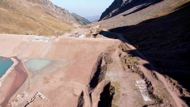 A mountain artificial lake with blue water and a dam. The turquoise surface of the water reflects the mountains. There is a small lake with muddy water nearby. Self-protective dam in the mountains - Footage, Video