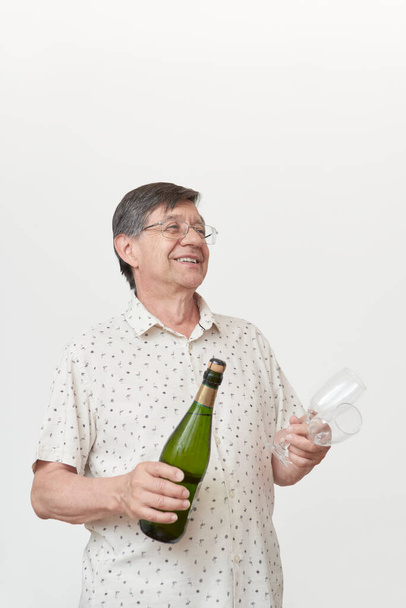 Uomo anziano ispanico sorridente mentre tiene in mano una bottiglia di champagne o sidro e un paio di bicchieri. Concetto di brindisi celebrativo. - Foto, immagini