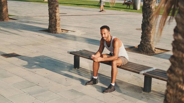Genç sakallı erkek sporcu antrenmandan sonra dinleniyor, bankta oturuyor, akıllı telefon kullanıyor.  - Fotoğraf, Görsel