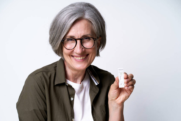 Happy grey haired mature woman showing covid-19 self test, excited of negative result wearing casual green shirt isolated on white background. Health care and medical concept.  - Photo, Image