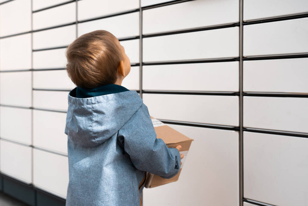Child parcel, boy using self service parcel terminal machine to send or receive package. Parcel delivery, pickup point with lockers, kid with parcel, contactless pack delivery. - Фото, зображення