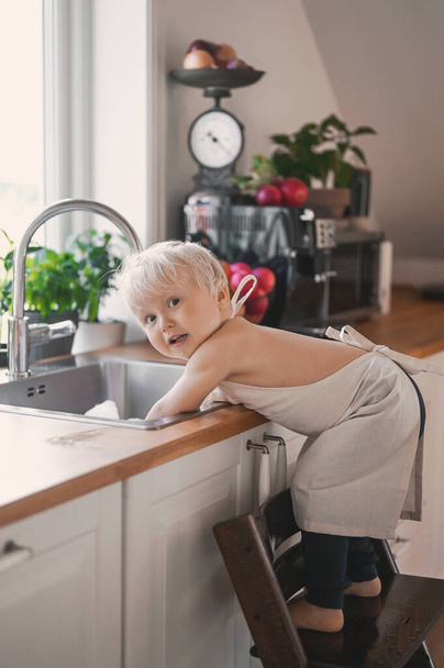 close up portrait of adorable cute baby boy washing dishes in the sink with foam and soap bubbles. - Foto, imagen