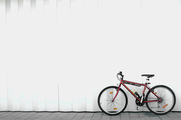 Μονόκλινο κόκκινο ποδήλατο βουνού χωρίς ανθρώπους που βρίσκονται στην κάτω δεξιά πλευρά της εικόνας και ακουμπά σε ένα λευκό τοίχο με μερικές μαύρες ρίγες και με χώρο για κείμενο στην κορυφή - Φωτογραφία, εικόνα