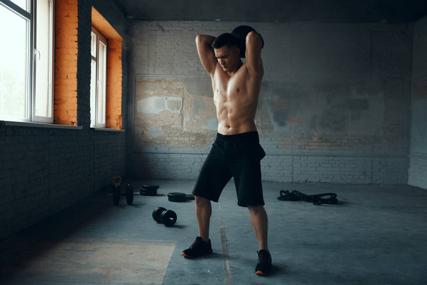 Full length of handsome young man exercising with medicine ball in gym - 写真・画像