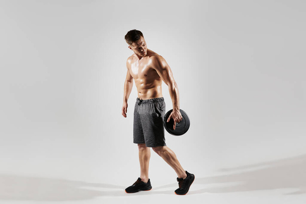Young fit man with perfect body holding medicine ball against white background - Foto, Imagen