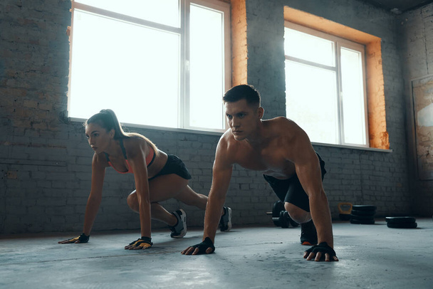 Young fit couple looking concentrated while exercising in gym together - Photo, image