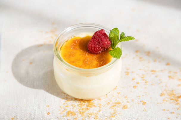 Fresh creme brulee dessert decorated with fresh berries and mint on a linen tablecloth in bright sunshine - Foto, Bild