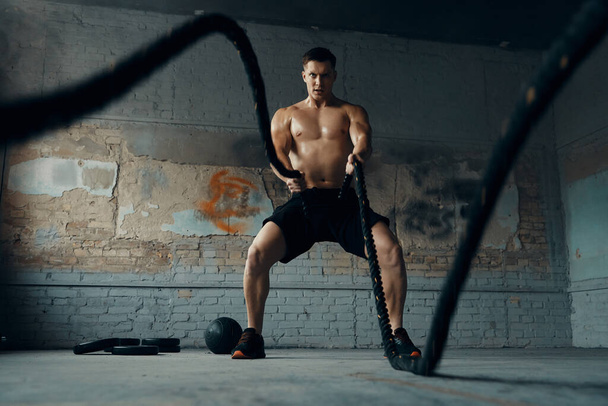 Confident young man exercising with battle rope in gym - Fotoğraf, Görsel