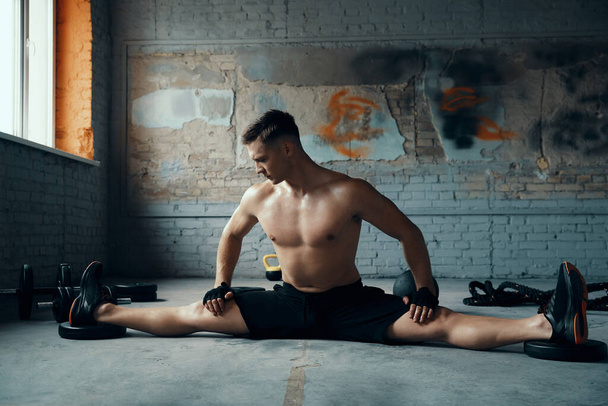 Confident young man doing the splits while exercising in gym - 写真・画像