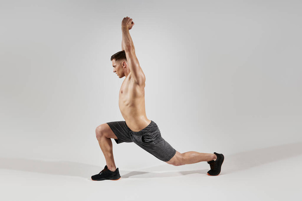 Confident fit man with perfect body doing stretching exercises against white background - Zdjęcie, obraz