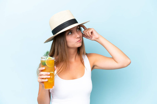 Nuori kaunis nainen, jolla cocktail eristetty sinisellä taustalla, jolla on epäilyksiä ja sekava ilme - Valokuva, kuva