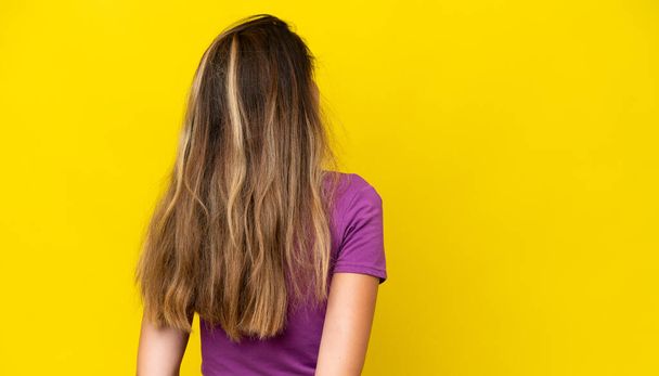 Young caucasian woman isolated on yellow background in back position and looking back - Fotoğraf, Görsel
