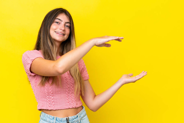 Young caucasian woman isolated on yellow background holding copyspace to insert an ad - Foto, Imagem