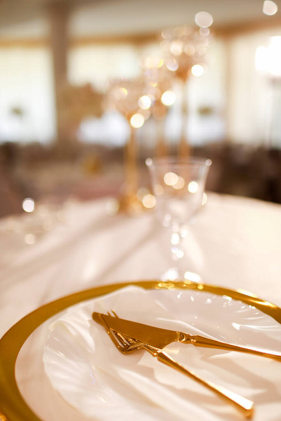 Tischdekoration mit rosa Tischdecke, Kristall-Kerzenständer mit Kerzen und weiße rosa Blumen im Restaurant. stilvoller Hochzeitstag. Decktisch mit Goldteller, Gabel und Messer. - Foto, Bild
