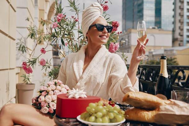 Happy woman in bathrobe enjoying champagne while having brunch on the balcony - Foto, imagen
