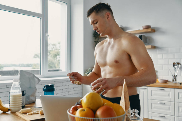 Young fit man preparing healthy food while standing at the kitchen - Fotografie, Obrázek