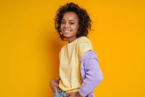 Beautiful African woman looking at camera and smiling while standing against yellow background - Valokuva, kuva