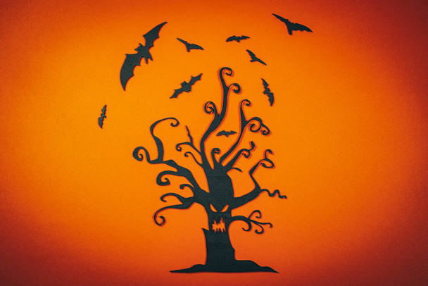 Halloween schwarz geschnitzter Baum mit fliegenden Fledermäusen auf orangefarbenem Hintergrund.. - Foto, Bild