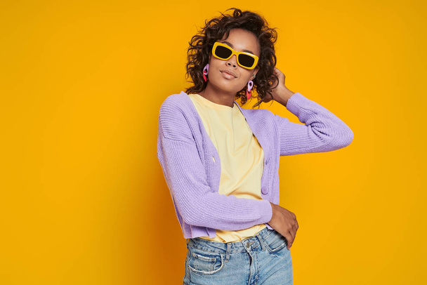 Beautiful African woman in funky eyeglasses standing against yellow background - Photo, Image