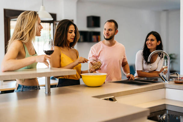4 amigos charlando en un mostrador de cocina mientras preparan comida. Alimento saludable - Foto, imagen