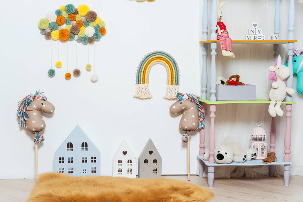 witte boekenkast in de kinderkamer met speelgoed. lichte kamer voor een kind met speelgoed van paarden en houten huizen. fotozone voor kinderen in de fotostudio - Foto, afbeelding